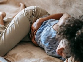 Como Diminuir as Cólicas Menstruais: 12 Formas Naturais e Eficazes Mulher deitada segurando a barriga com dor de cólicas menstruais