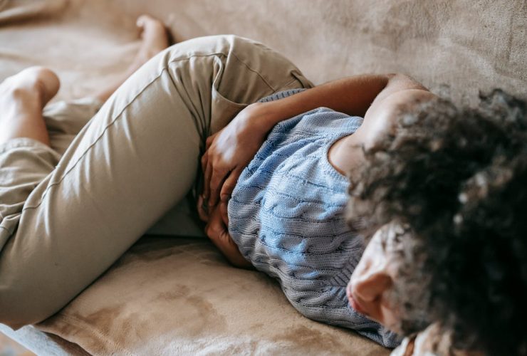 Como Diminuir as Cólicas Menstruais: 12 Formas Naturais e Eficazes Mulher deitada segurando a barriga com dor de cólicas menstruais