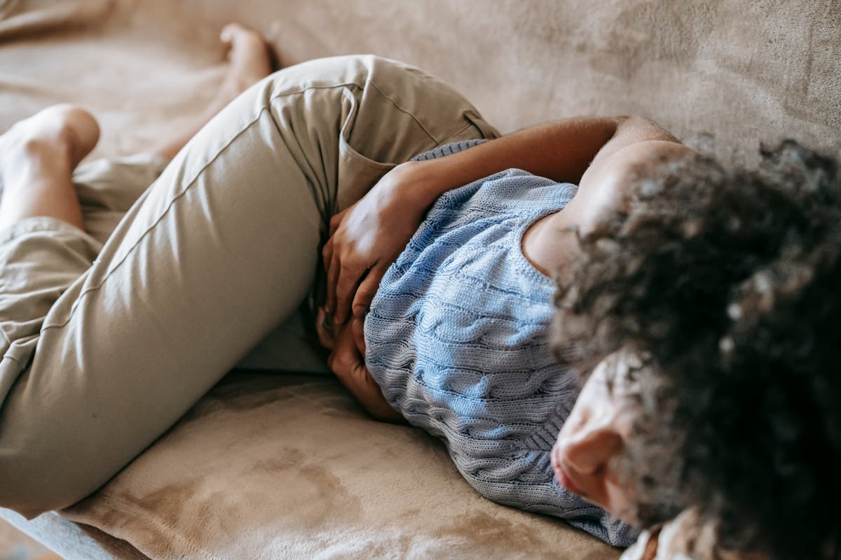 Mulher deitada segurando a barriga com dor de cólicas menstruais